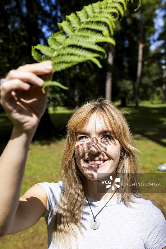 快乐的年轻女性在阳光明媚的日子里手持蕨类植物叶子图片素材