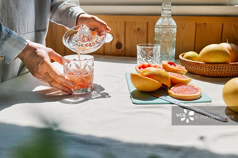 匿名女性在厨房里将新鲜的葡萄柚汁倒入饮用杯中。图片素材