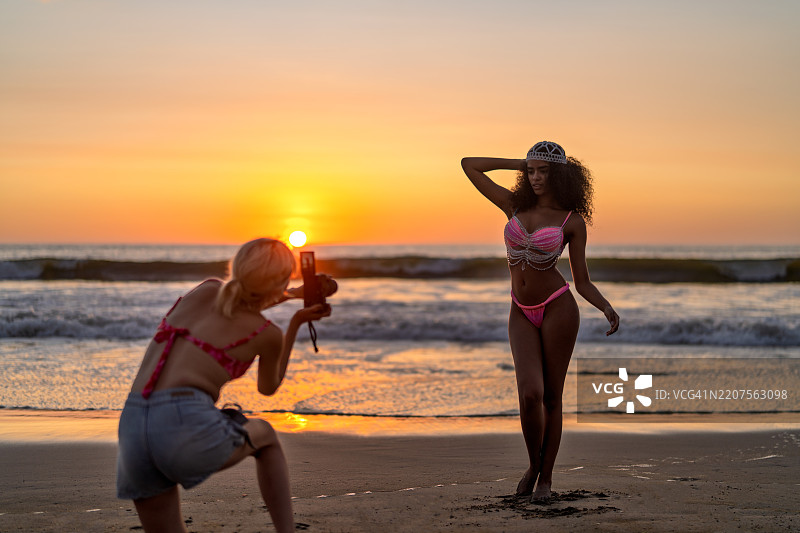 摄影师在海滩日落时为模特拍照图片素材