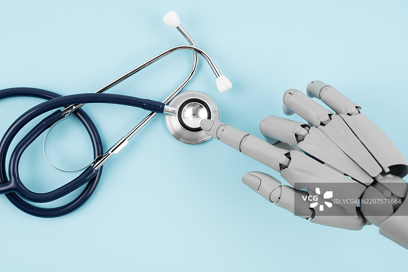 蓝色背景上的机器人手指玩具和医疗听诊器，人工智能和智能技术在医学和诊断中的概念。图片素材