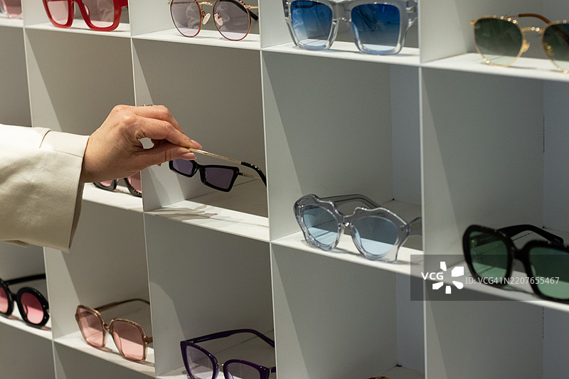 在眼镜店的展示柜中手动挑选太阳镜图片素材