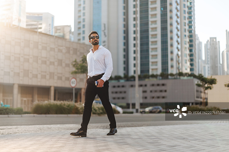 自信的年轻中东男性在迪拜穿着白衬衫和黑裤子走路图片素材