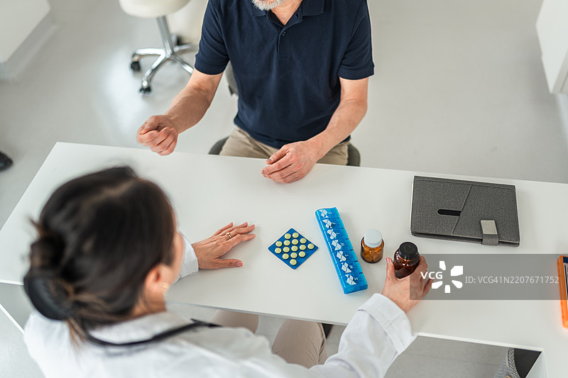 亚洲男性在医生办公室与女性医疗专业人员讨论药物治疗图片素材