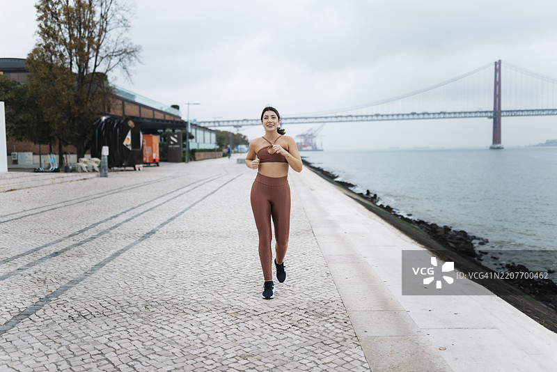 年轻的运动女性在里斯本的河边跑步图片素材