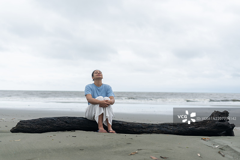 平静的女人坐在海岸上，深呼吸，仰望天空。图片素材