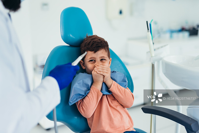 害怕的孩子在牙医预约时用手捂住嘴巴图片素材