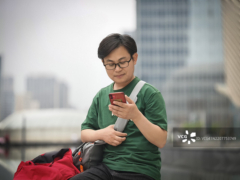 亚洲帅气年轻男子在城市街道上使用智能手机图片素材