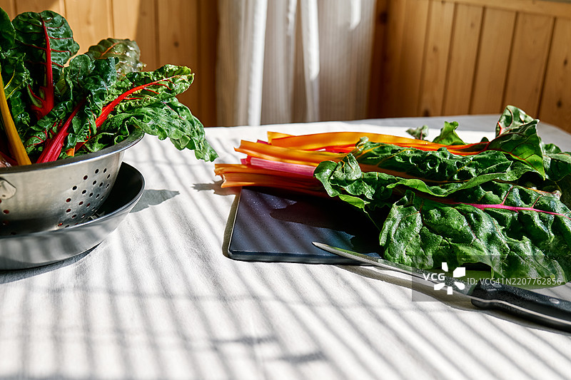 瑞士甜菜或芥菜叶放在桌子上的切菜板上，桌上铺着亚麻桌布。图片素材