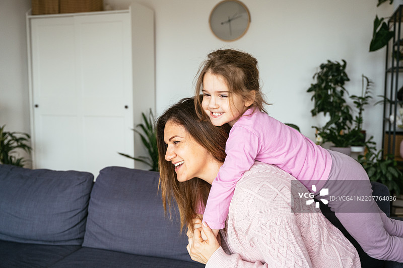 母女在家中玩耍和亲密互动。女孩抱着母亲，玩骑背游戏。图片素材