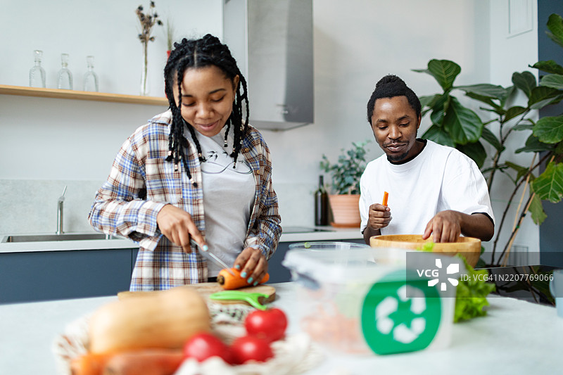 年轻情侣在切菜，并将菜皮放入回收箱进行堆肥处理图片素材