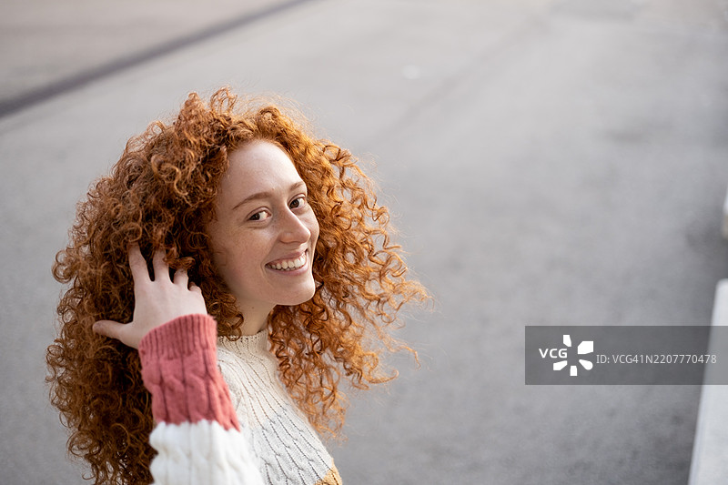 年轻的红发女性在城市户外转身看向镜头。留白空间。图片素材