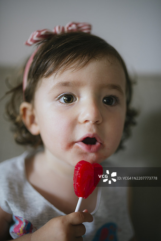 可爱的小女孩在家里吃着心形棒棒糖图片素材