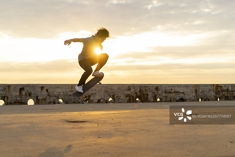 年轻的中国男子在海滩附近的日出时分滑板。图片素材