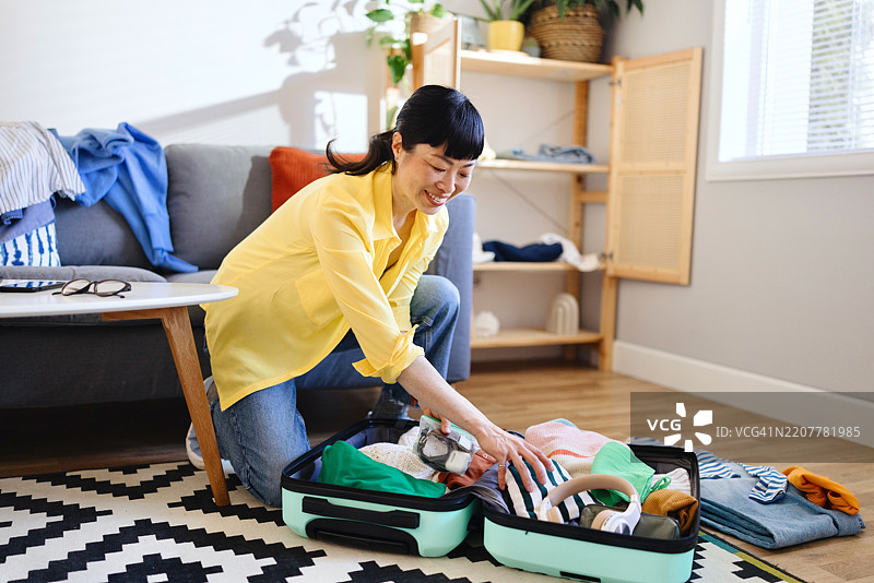 微笑的日本女性正在把衣服放进行李箱里图片素材