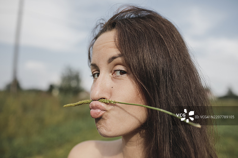 女人用嘴巴平衡植物茎的肖像图片素材