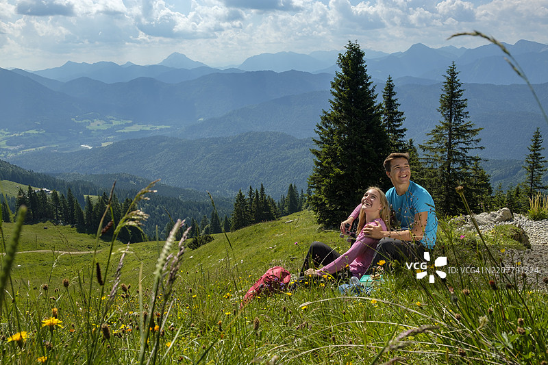 德国，巴伐利亚，莱格里斯附近的布劳内克，快乐的年轻情侣在阿尔卑斯山的草地上休息图片素材