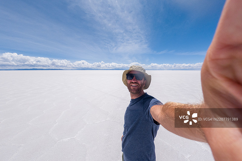 男子在广阔的盐滩上拍自拍，背景是晴朗的蓝天图片素材