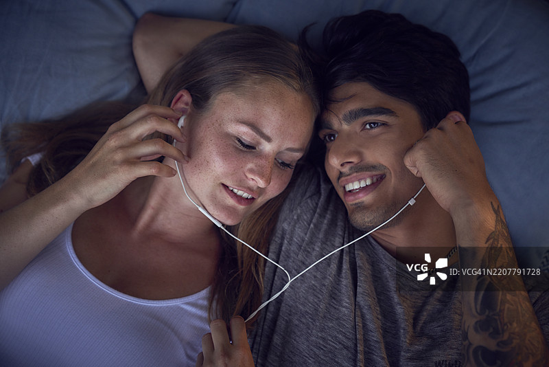 年轻情侣躺在垫子上，分享耳机，听音乐图片素材