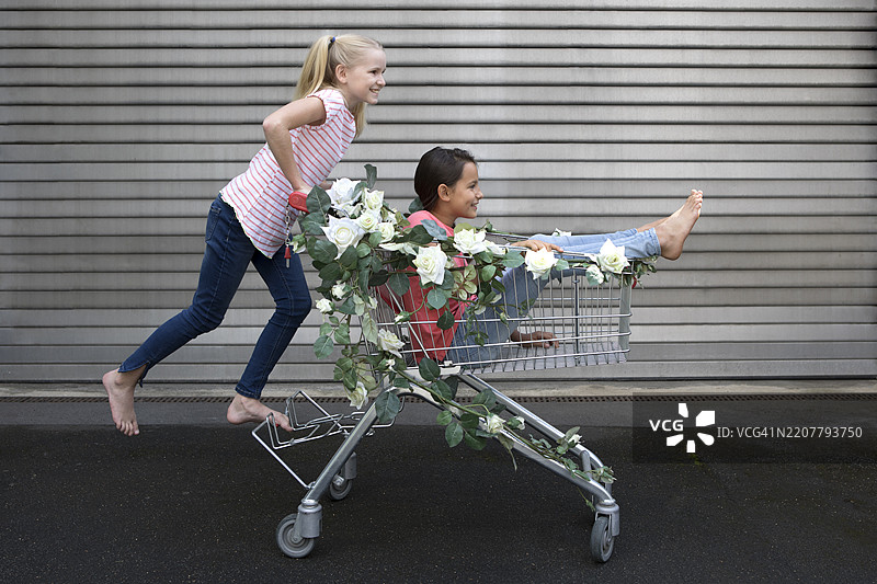 两个女孩在玩装饰有假花的购物车图片素材