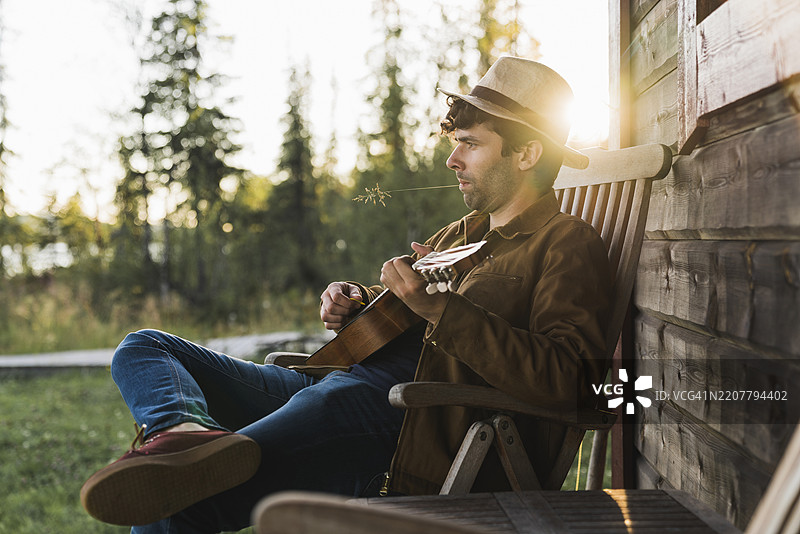 年轻男子坐在木屋的阳台上弹奏尤克里里图片素材