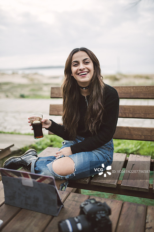 坐在户外长椅上的年轻女性，手持相机和平板电脑，面带笑容。图片素材
