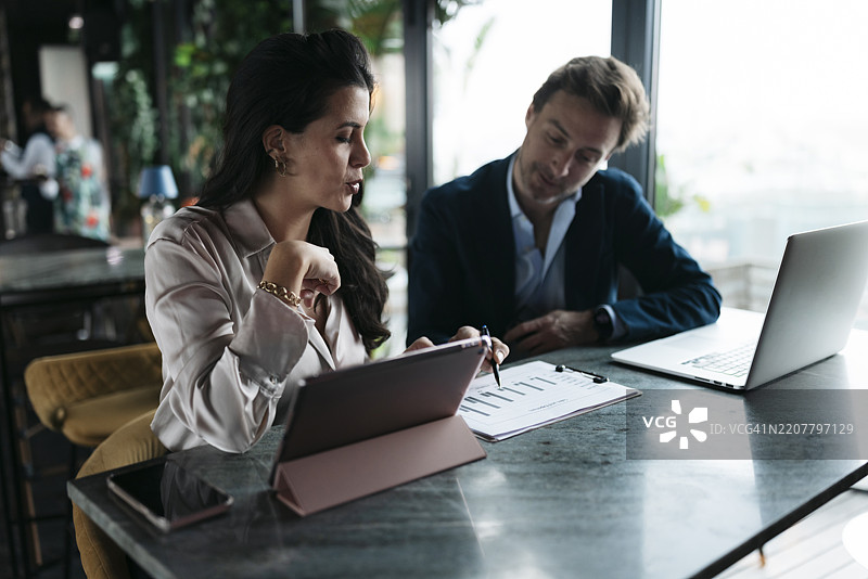 商务人士在餐厅分析纸质和数字平板上的财务图表图片素材