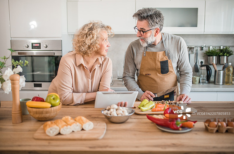 一名男子正在切菜并准备烹饪的食材，而一名女子则在为他朗读她在网上找到的菜谱。图片素材