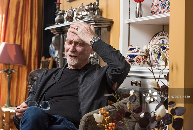 老年男性在客厅里用手扶着头图片素材