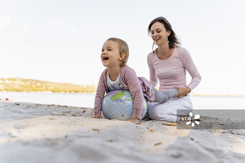 母亲和小女儿在海边一起玩地球沙滩球图片素材