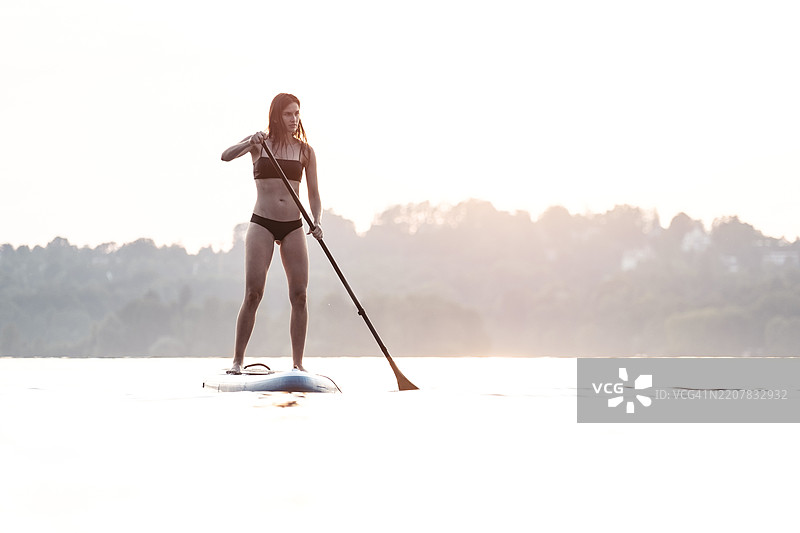 年轻女性在德国斯塔恩贝格湖日落时进行立式划水运动图片素材