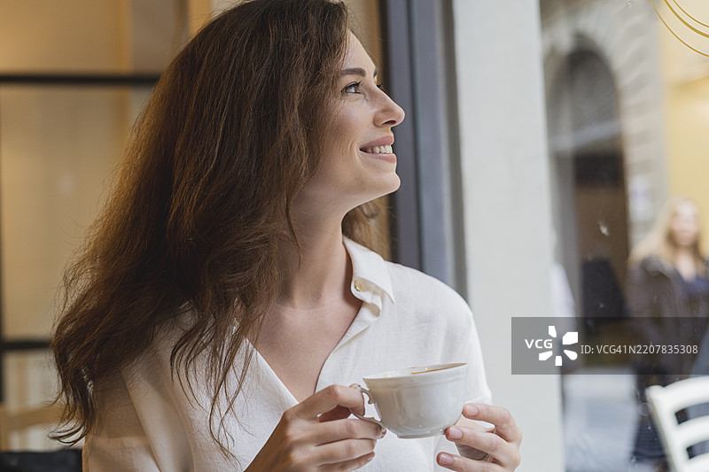 快乐的年轻女性在咖啡馆里望向窗外图片素材