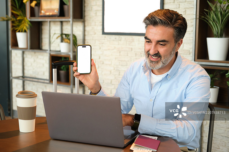 微笑的商人在机场休息室进行视频通话时展示带有空白屏幕的智能手机图片素材