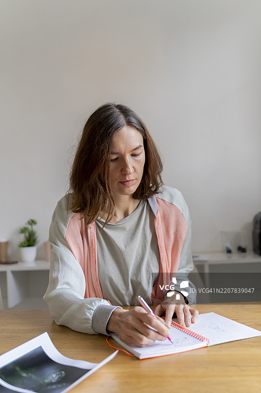 女在办公室的桌子上写笔记本。图片素材