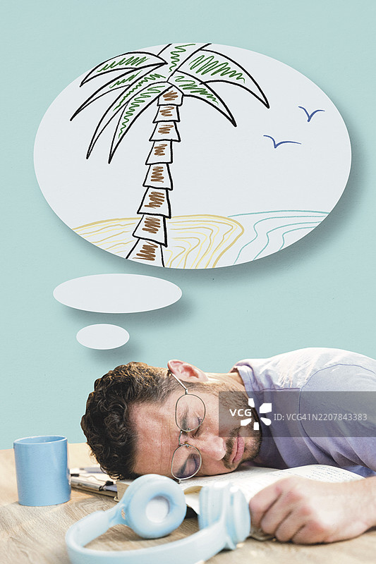 疲惫的办公室工作人员在桌子上睡着，头靠在书本上，梦见热带海滩和棕榈树。图片素材