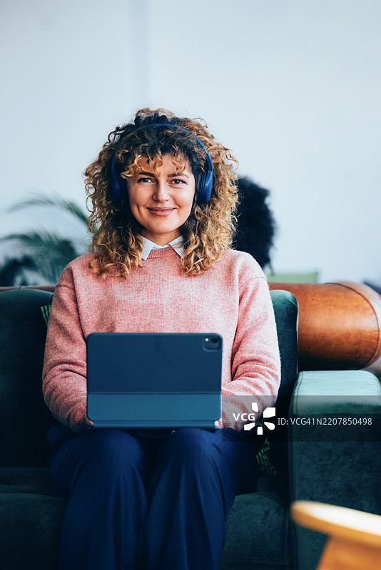 微笑的女性在家中戴着耳机使用平板电脑图片素材