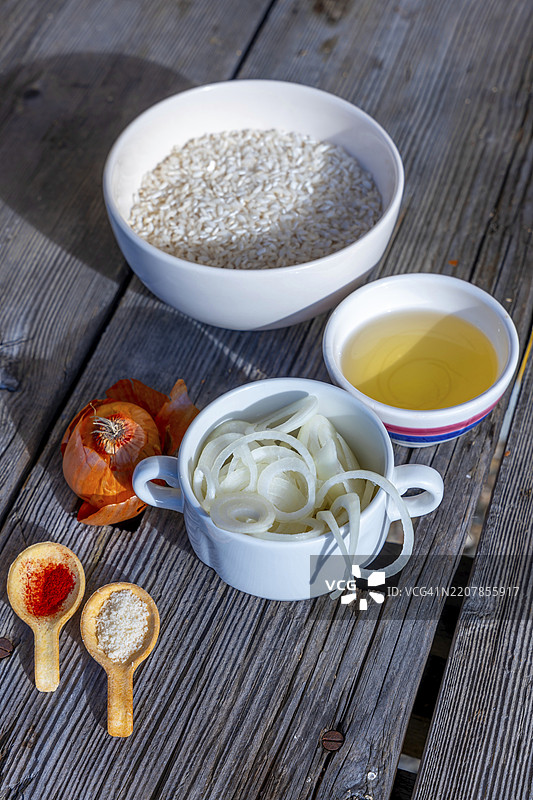 制作藏红花米饭的原料，米兰式烩饭，配有帕尔马干酪、白葡萄酒和洋葱，摆放在瑞士提契诺州卢加诺的一张古老木桌上，阳光洒在上面。图片素材