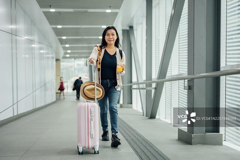 在移动：一位快乐的亚洲女性在步行道上拖着行李图片素材
