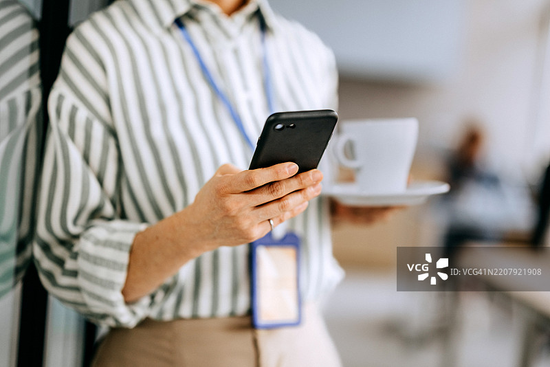 女性企业家在办公室里一边拿着咖啡杯一边用手机发短信的特写镜头图片素材