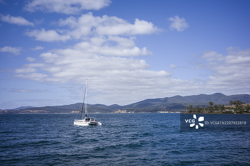 在蓝天背景下，船只在海洋中航行，穿越塔斯马尼亚的玛丽亚岛，远处是山脉。图片素材