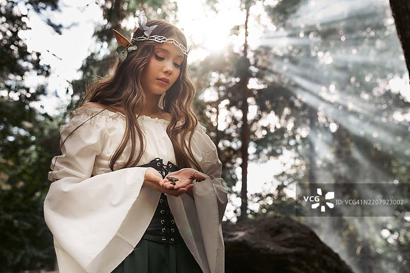 身着复古服装的精灵女性肖像，手持一把旧钥匙站在森林中。图片素材