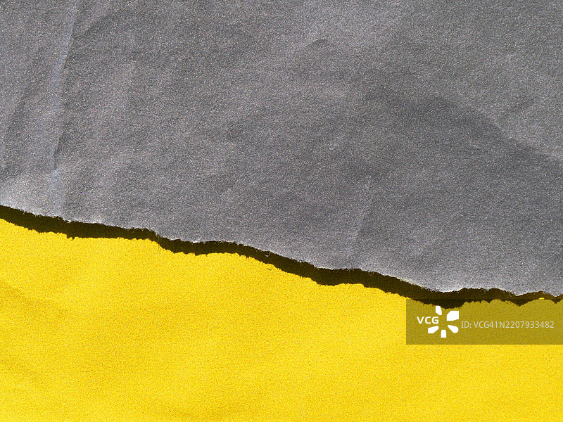 撕裂的灰色纸张和明亮的黄色纸张特写，带有阴影。粗糙的纹理。阳光，自然色彩。图片素材