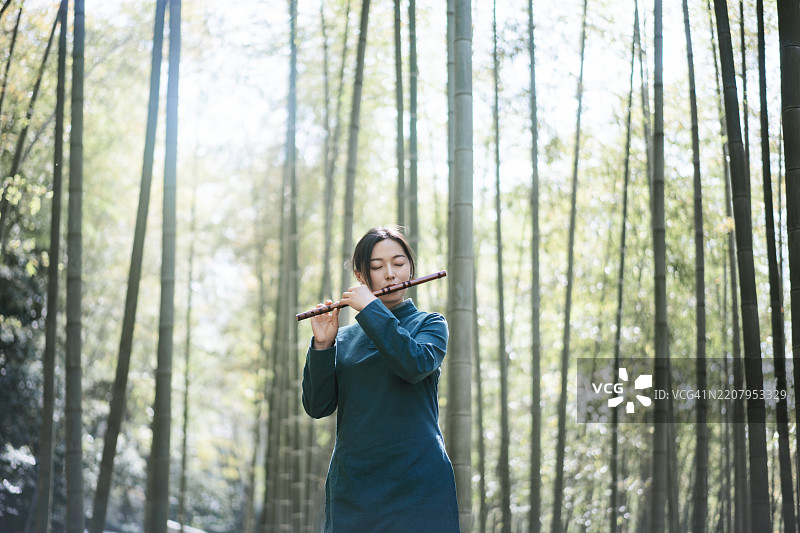 身穿传统服装的亚洲女性在竹林中吹奏笛子图片素材