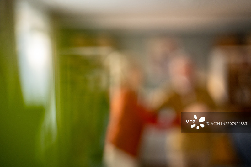 模糊的图像，显示人们在有绿色窗帘和温暖灯光的房间里聚集。图片素材