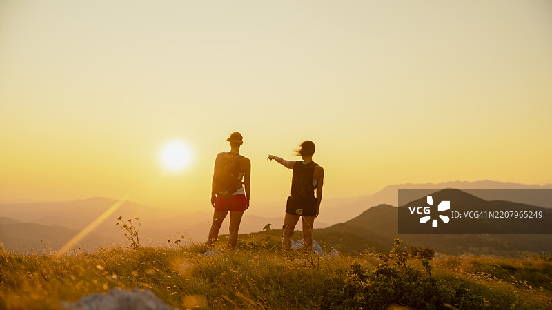 两位女性在山脊上指着壮观的日落景色图片素材
