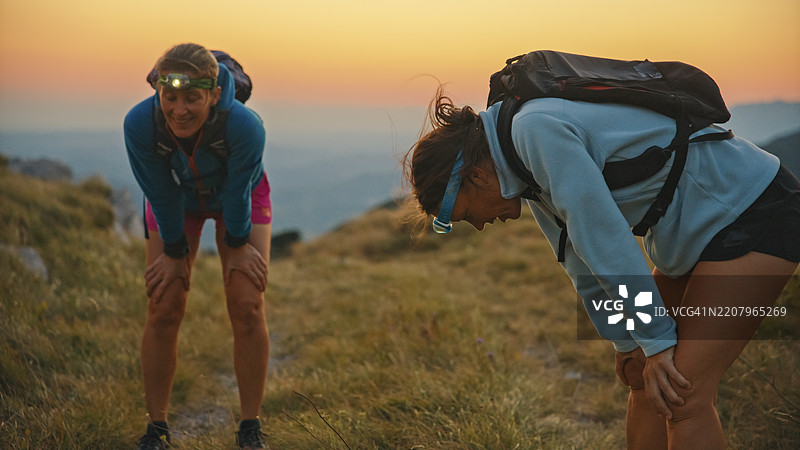 疲惫的女性越野跑者在日落时分的山上休息，头灯照亮周围图片素材