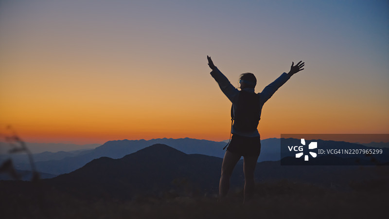 女人在黄昏时分庆祝登顶山峰图片素材