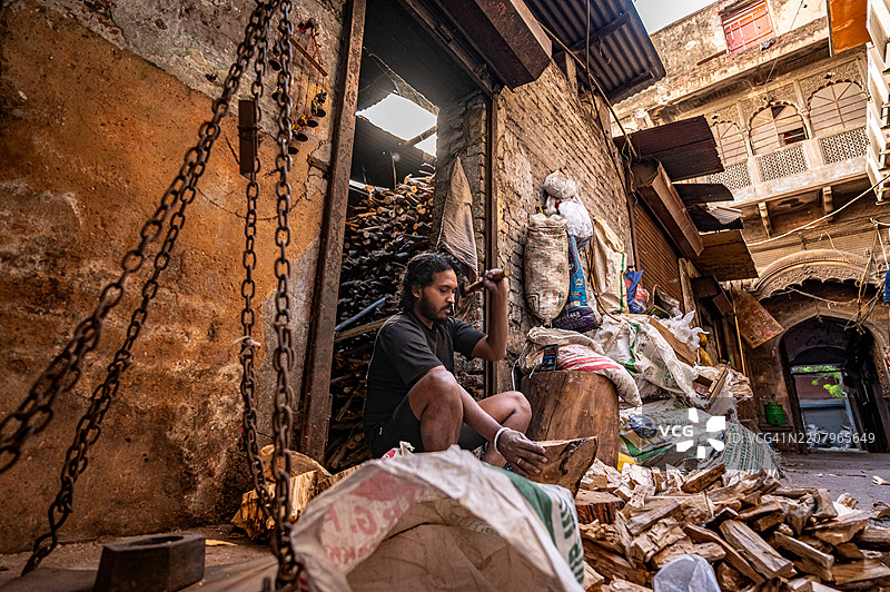 一名工人在德里老城区的昌迪乔克切割小木材，以便在传统木炭厂开始燃烧过程。图片素材