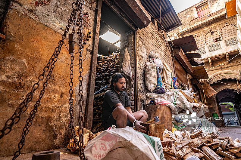 一名工人在德里老城区的昌迪乔克切割小木材，准备在传统木炭厂开始燃烧过程。图片素材