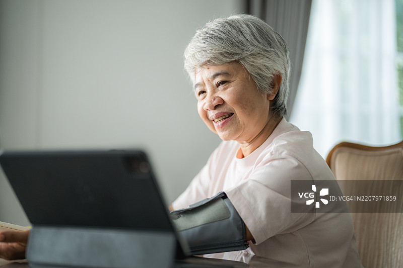一位老年女性正在通过数字平板学习如何使用血压监测仪图片素材