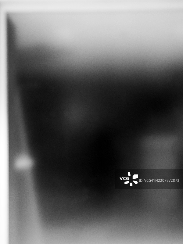 在阴影与光线之间，透过一扇不透明的窗户看到的黑暗房间。逆光。黑白。自然光。加拿大魁北克省蒙特利尔。图片素材